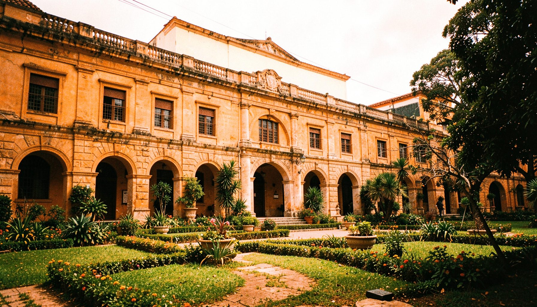 Fotografía de las instalaciones exteriores de la universidad con fachada de estilo colonial, arcos de piedra y jardines verdes